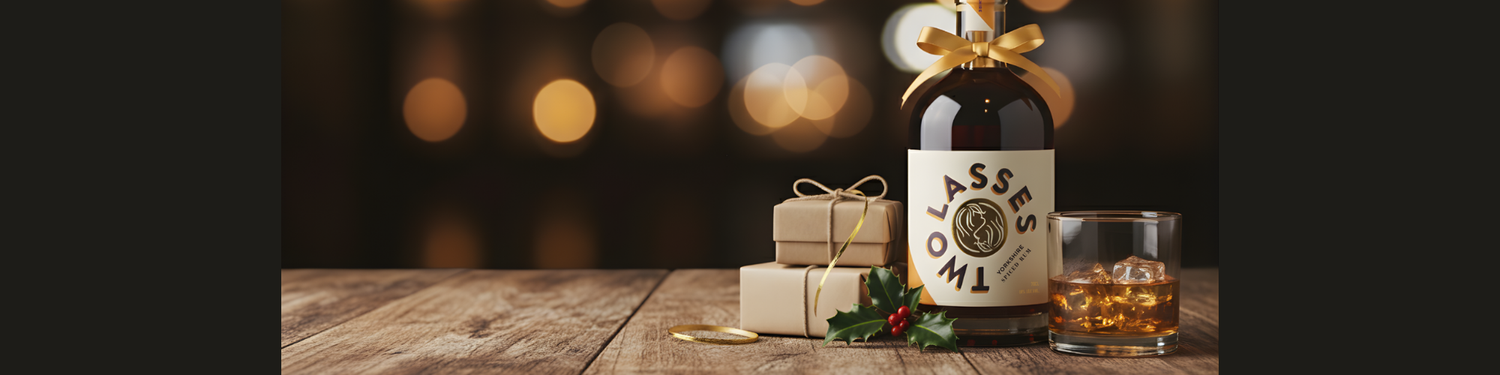 Bottle of Two Lasses Yorkshire Spiced Rum with Christmas gifts and holly on a wooden table.